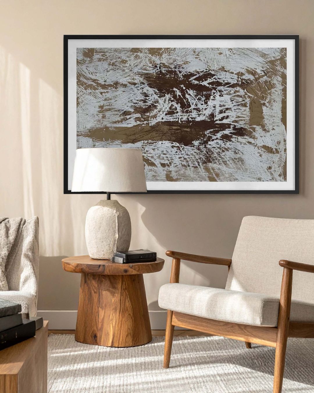 Framed brown and beige abstract artwork in a sunlit living room with a cream armchair